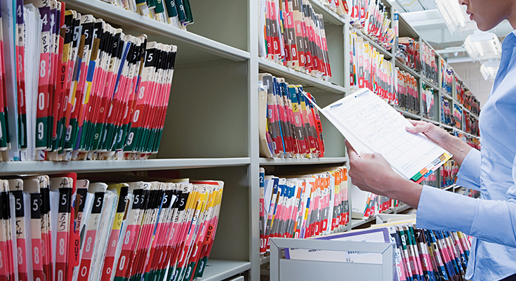 Someone standing in front of library of patient files, looking at a patient's chart