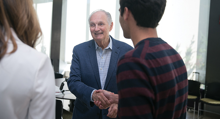 Alan Alda smiling, shaking hands with someone