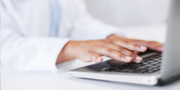 Close-up shot of physician's hands on laptop keyboard