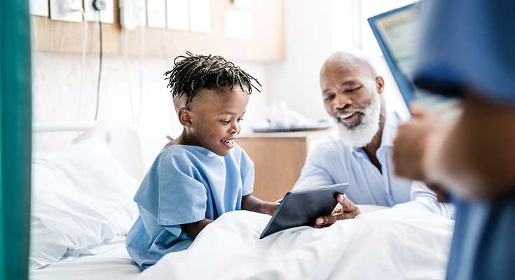 A child using a tablet in a hospital bed with the help of an adult man