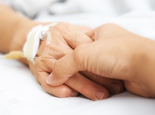 Two people holding hands, one has an intravenous line