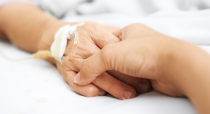 Two people holding hands, one has an intravenous line