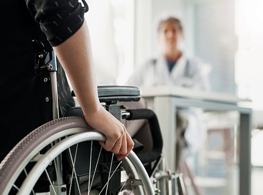 Photo of someone in a wheelchair from behind approaching a physician
