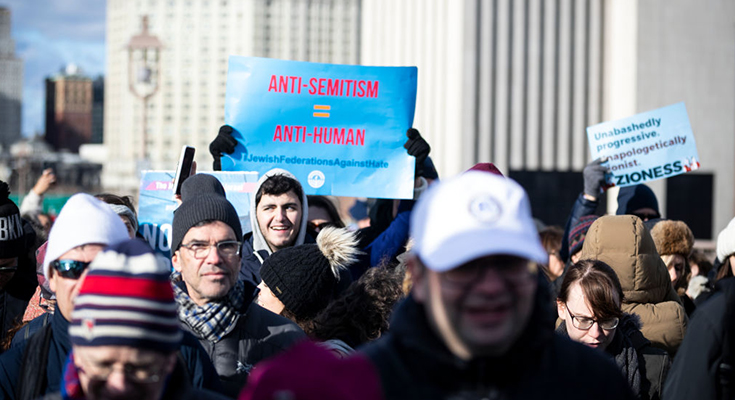 Manhattan, NY — January 05: A marcher holds a sign that reads "Anti-Semitism = Anti-Human" as they walk across the Brooklyn Bridge.