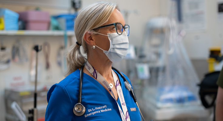 A physician, Dr. Laura Foxcroft, wears a mask in a hospital room.