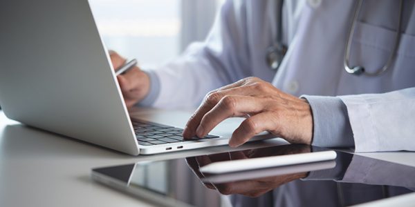 A physician types on a laptop