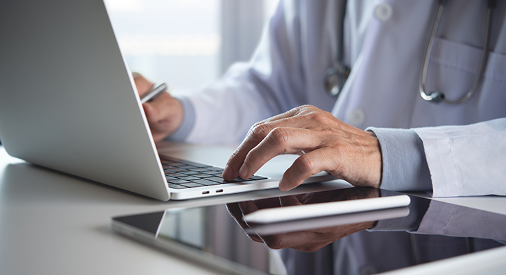 A physician types on a laptop