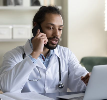 A physician on a phone using a laptop.
