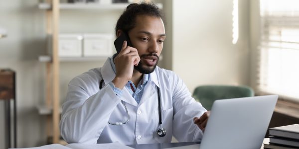 A physician on a phone using a laptop.